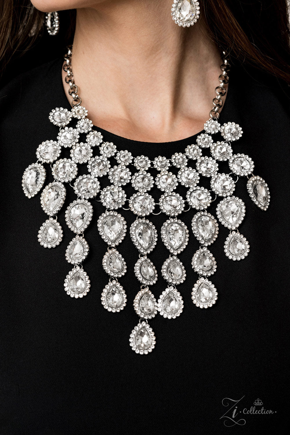 tem #Z916 Encrusted in dainty white rhinestone frames, columns of glassy white gem studded frames increase in size as they drip below the collar. Varying in size and number, white rhinestone encrusted teardrop gems link together as they trickle down the chest , creating a plunging fringe for a ,mesmerizing finish. Features an adjustable clasp closure. Sold as one individual necklace. Includes one pair of matching earrings.
