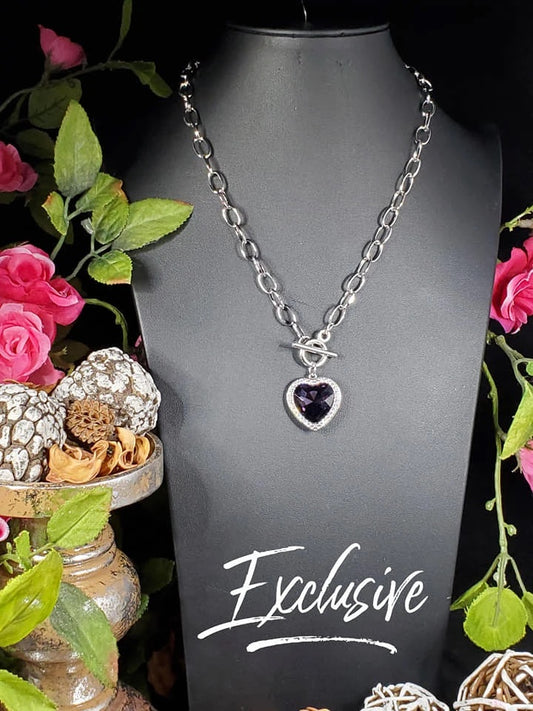 Featuring a purple gem encrusted in a heart shaped pendant, surrounded by white rhinestones. Features a toggle closure. Sold as one individual necklace. Includes one pair of matching earrings.